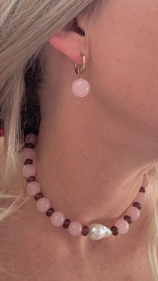 Close-up of a person wearing a beaded necklace and pink hoop earrings.