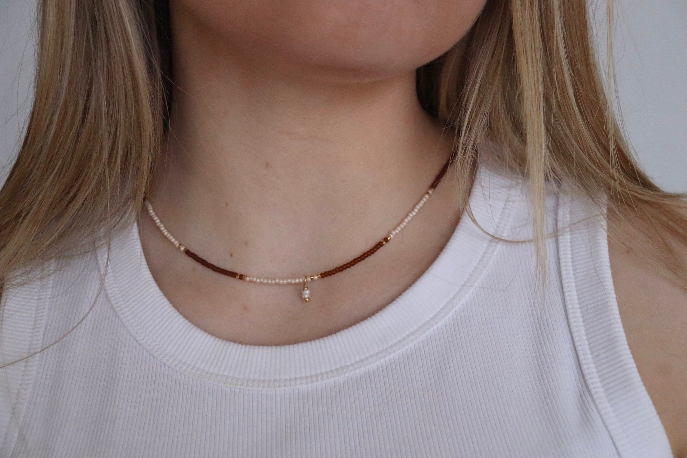 Close-up of a person wearing a delicate beaded rose and white necklace with a plain background and pearl detail